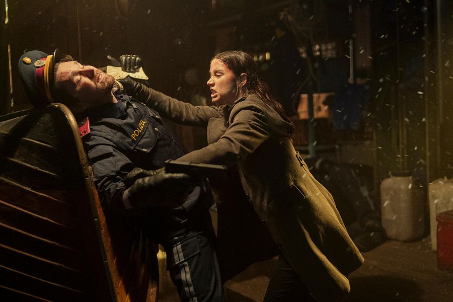 Ana de Armas agarra a un policía por el cuello en una escena de acción oscura y lluviosa de 'Ballerina'.  Su expresión es decidida, sugiriendo violencia y confrontación.