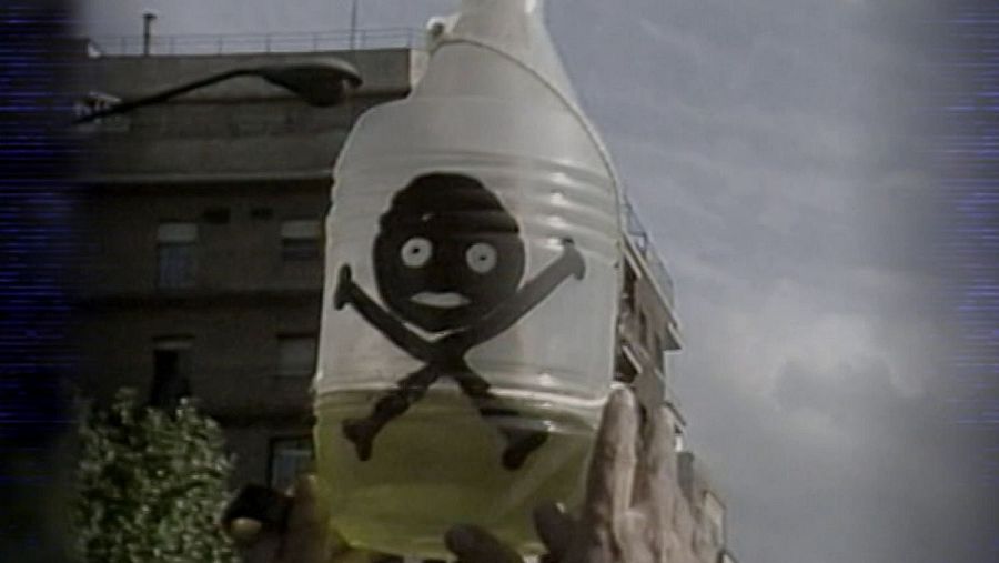 Imagen de una garrafa con líquido y etiqueta de calavera, sostenida por manos.  Simboliza el peligro del aceite de colza adulterado.