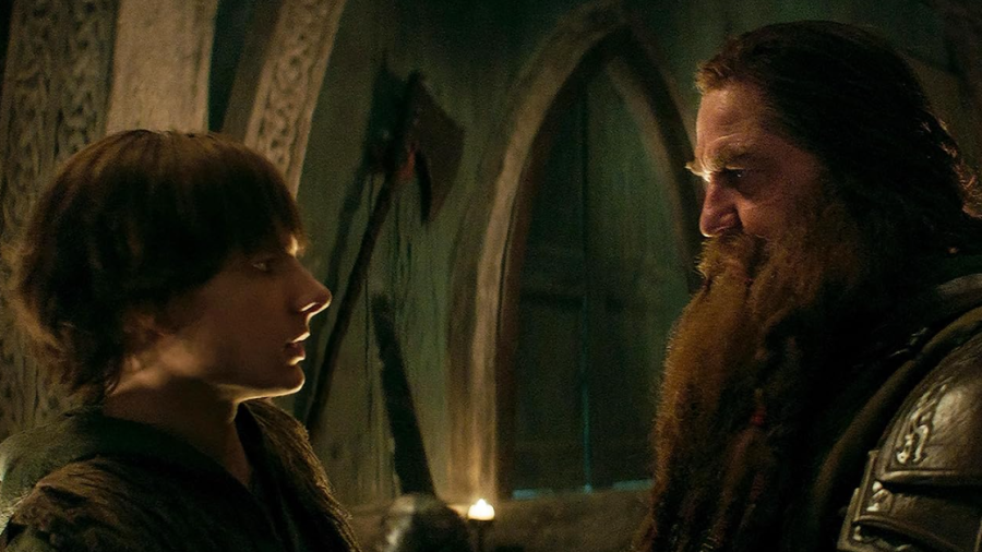 Escena dramática entre padre e hijo, con iluminación tenue y atmósfera tensa.  El hijo, de pelo oscuro, mira a su padre, de barba pelirroja y armadura.