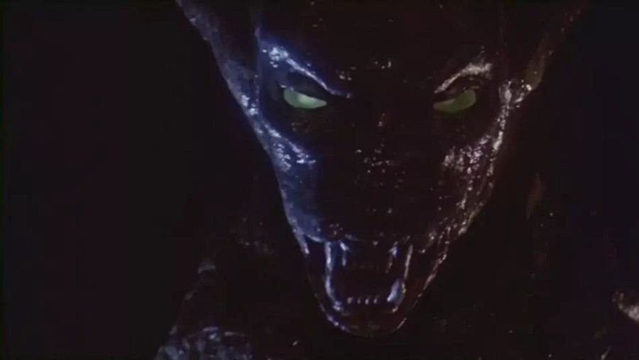 Monstruo de 'La galaxia del terror': piel oscura y viscosa, ojos verdes brillantes, dientes afilados, fondo negro.
