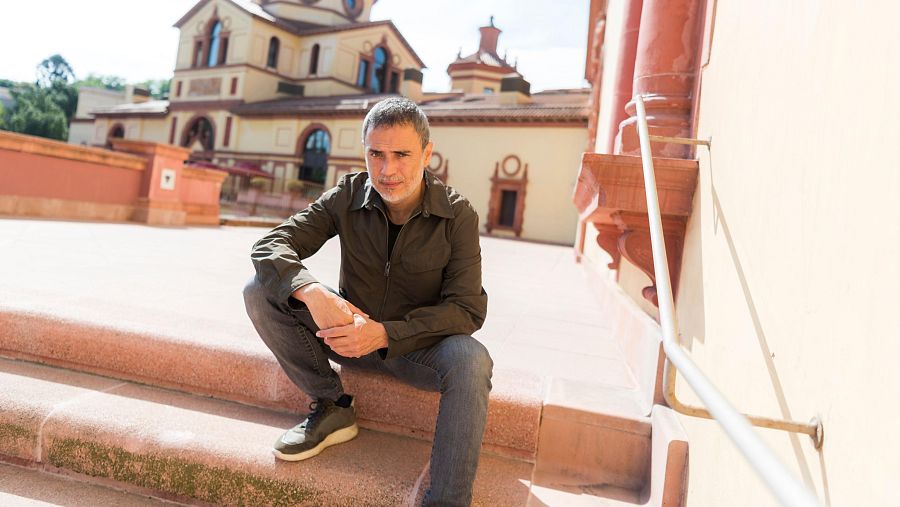 Julio Manrique assegut a unes escales amb l'edifici del Teatre Lliure al fons.