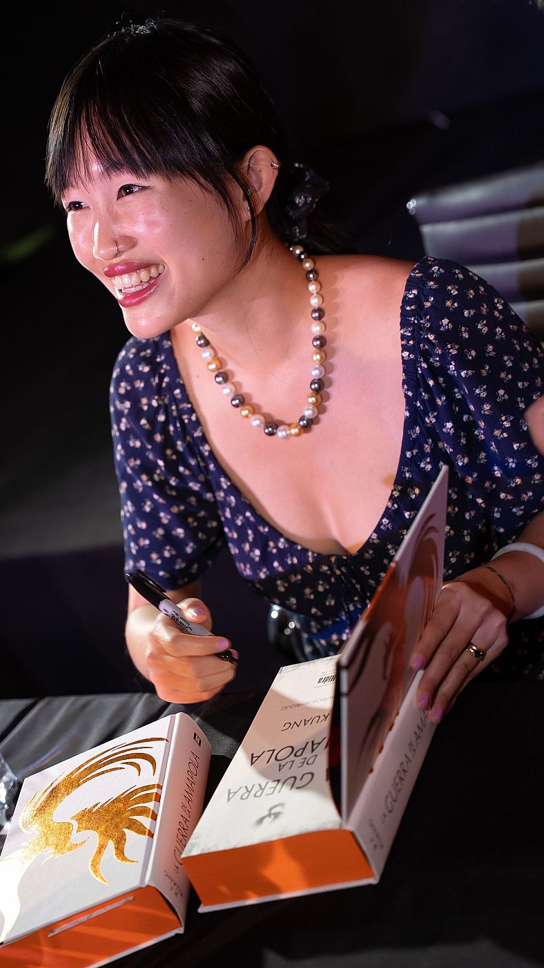 R. F. Kuang, sonriente, firma ejemplares de su libro 