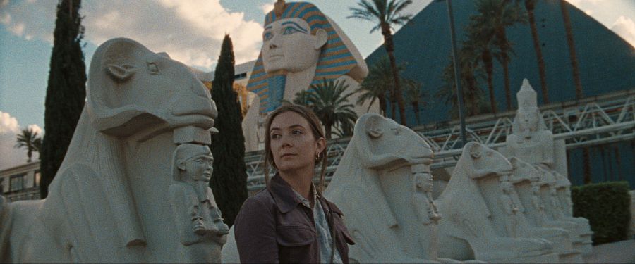 Mujer con chaqueta marrón entre esfinges de cabeza de carnero, en un decorado que recrea una atmósfera egipcia. Fotograma de 'The Last Showgirl'.