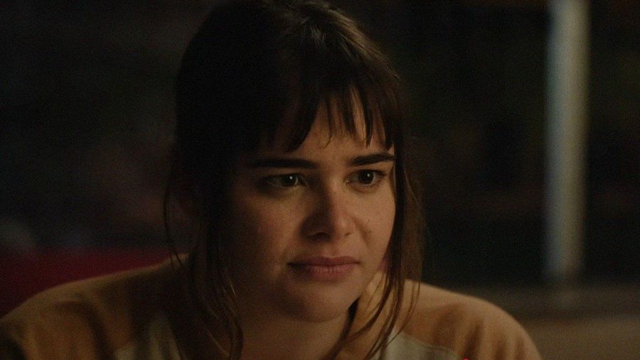 Mujer joven, cabello oscuro y flequillo, expresión seria, iluminación tenue, fondo oscuro. Fotograma de película.