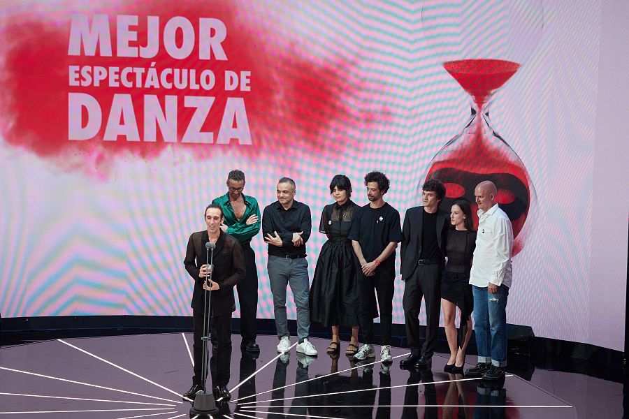 Entrega de premio a un grupo en un escenario con pantalla mostrando 