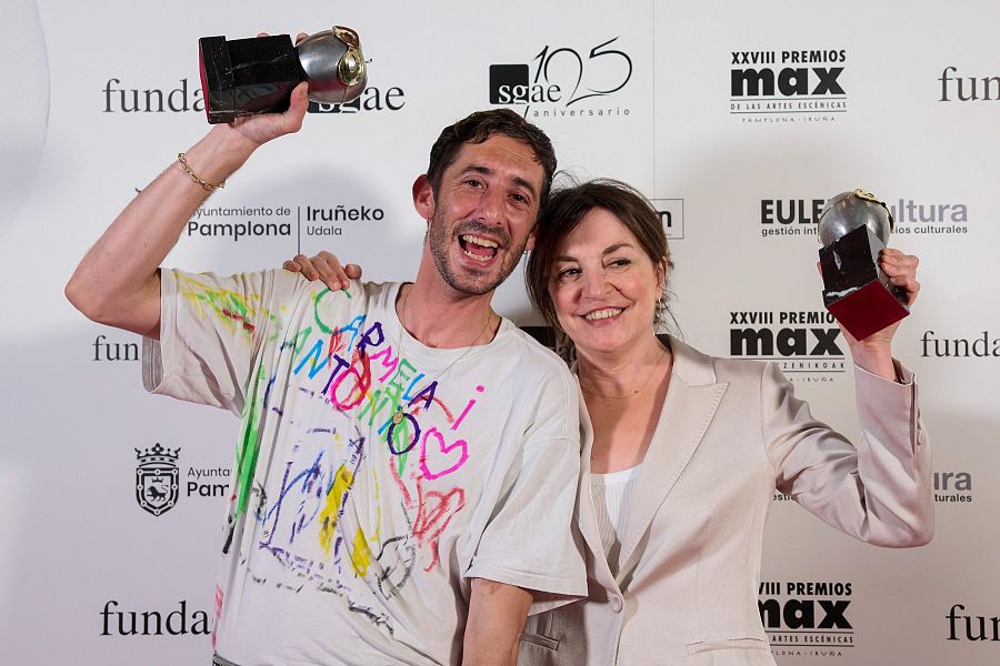 Dos actores, ganadores de premios, sonríen en un photocall. Él viste camiseta estampada y ella americana beige; ambos muestran sus galardones.