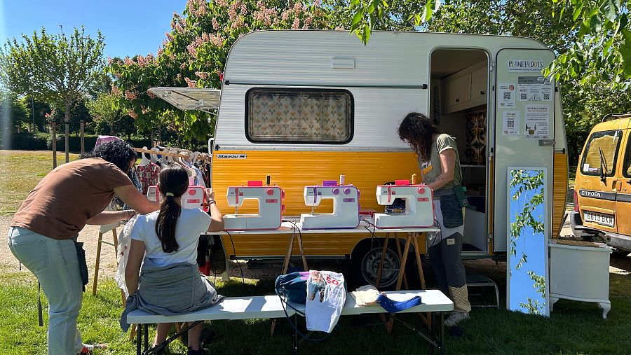 Taller móvil de costura sostenible: caravana amarilla y blanca con máquinas de coser, varias personas participando en un espacio verde.