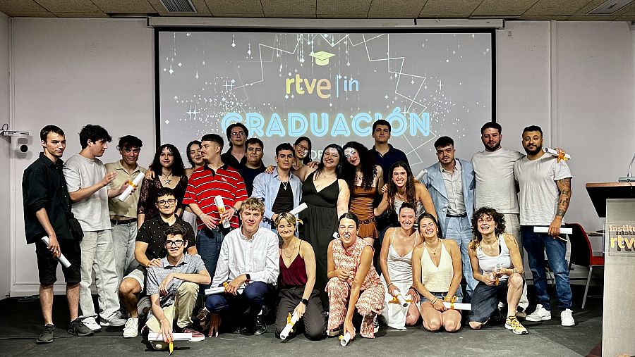 Graduados del Ciclo de Realización posan con sus diplomas en un auditorio, tras una ceremonia con la presencia del logo de RTVE Instituto.