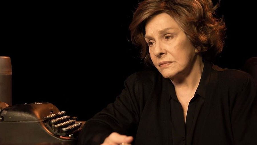 Retrato de Lola Herrera con el pelo corto castaño rojizo, expresión seria y blusa negra, junto a una máquina de escribir antigua.