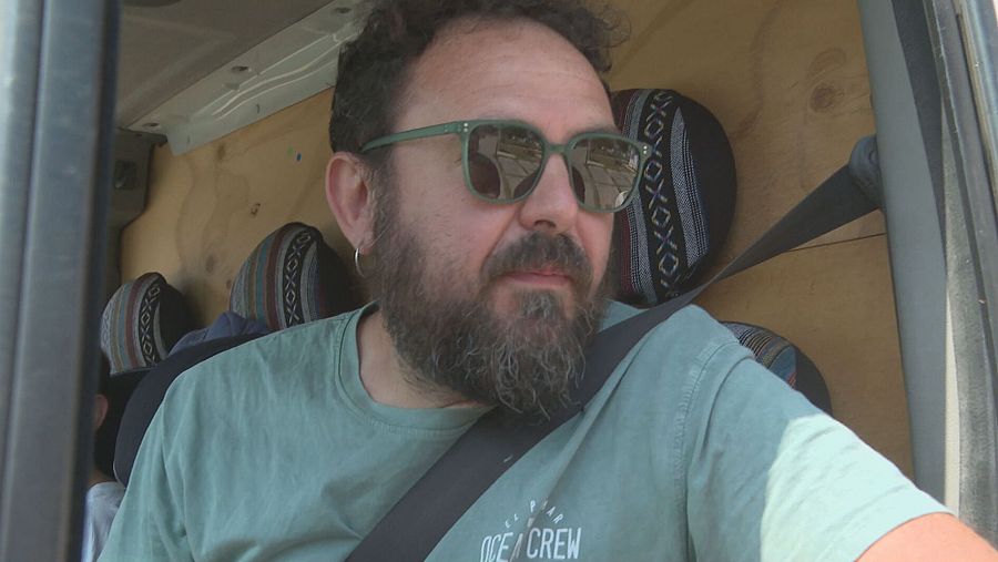 Hombre con barba y gafas de sol en autocaravana de madera, posiblemente dando testimonio sobre la criminalización de autocaravanistas.