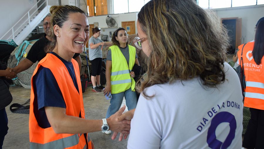 Encuentro en espacio amplio; mujer con chaleco naranja saluda a otra con camiseta 