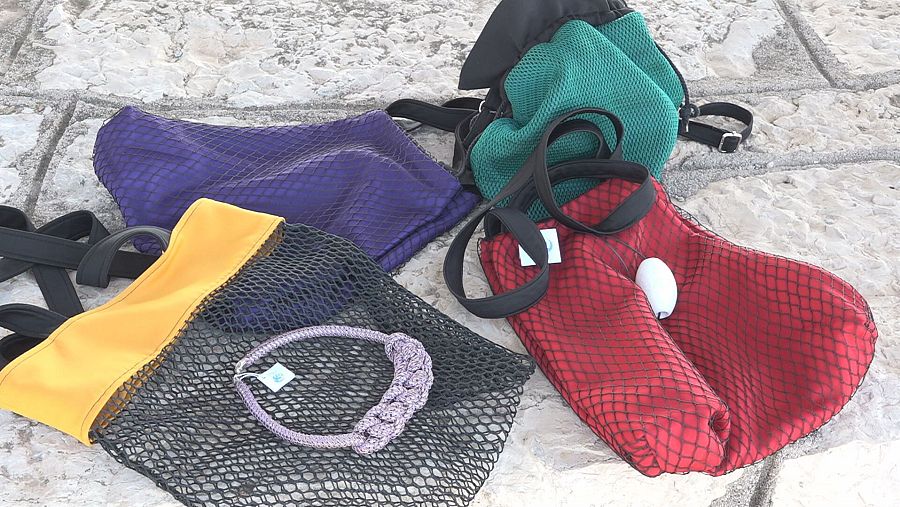 Bolsos de diversos colores y formas, elaborados con redes de pesca recicladas; algunos contienen objetos decorativos. Texturas variadas y asas visibles.
