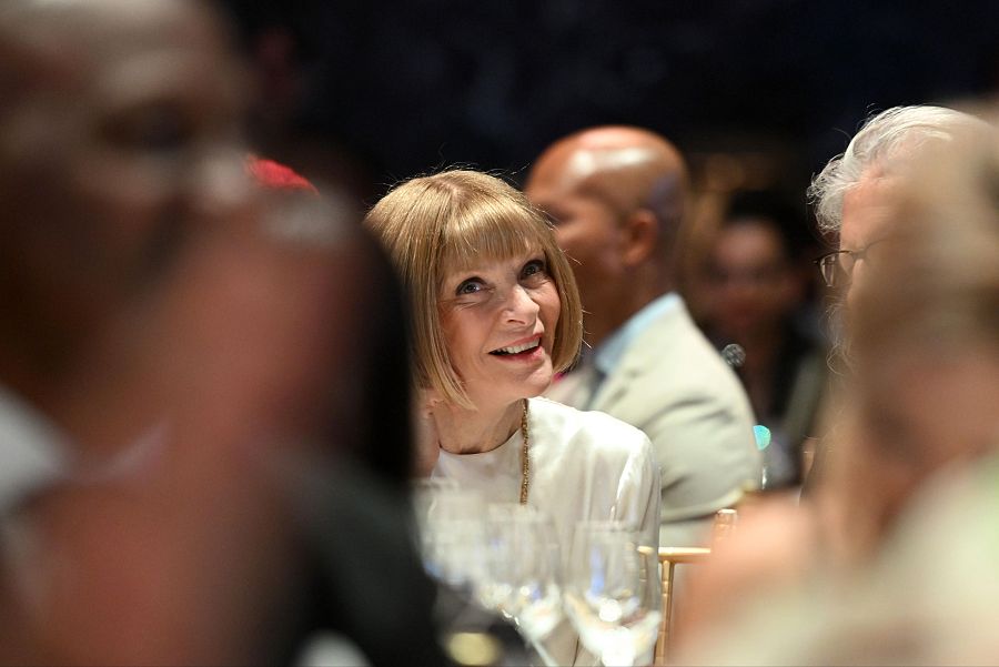 Anna Wintour en evento en Nueva York, mayo 2025.  Sentada a una mesa, con copa de vino cercana, expresión sonriente.