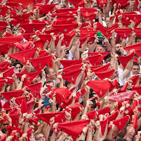 Multitud en celebración, vestida de blanco, ondeando pañuelos rojos.  Ambiente festivo y mucha gente con teléfonos móviles.