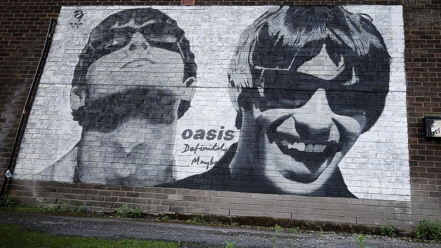 Mural en blanco y negro de los hermanos Gallagher de Oasis en Manchester.  Se muestran sus rostros con gafas de sol y el nombre de la banda, 