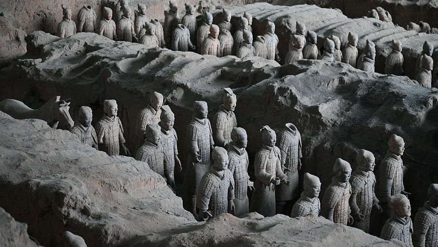 Guerreros de terracota de tamaño natural, en formación, dentro de una fosa de excavación.  Detalles únicos en sus posturas y expresiones faciales; algunos con caballos.