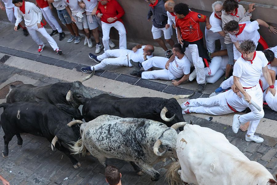 Toros de Cebada Gago corren por una calle estrecha en un encierro, con corredores intentando esquivarlos; algunos corredores han caído al suelo.