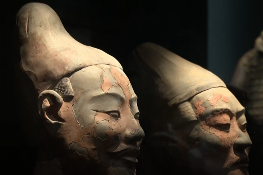 Primer plano de dos cabezas de figuras de terracota con restos de pigmentación, mostrando desgaste y detalles faciales. Iluminación que resalta la textura.