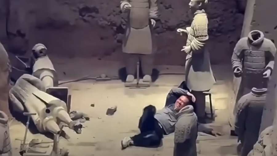 Interior de una fosa con guerreros de terracota. Un hombre en el suelo, cerca de un guerrero roto. Iluminación tenue.