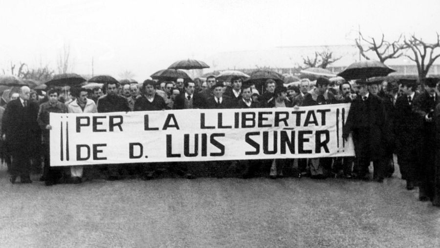 Multitud manifestándose bajo lluvia, con pancarta pidiendo la libertad de D. Luis Suñer. Fotografía en blanco y negro titulada 