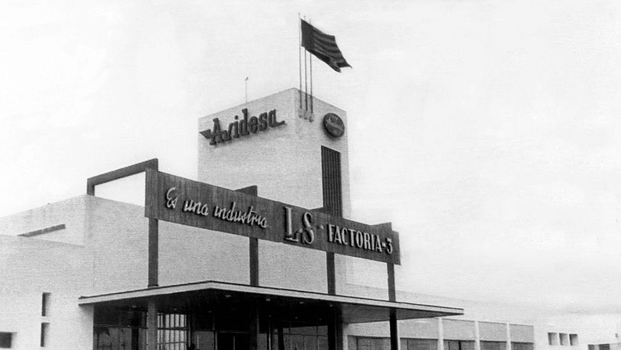 Fachada de fábrica antigua con rótulos, bandera española y las iniciales 