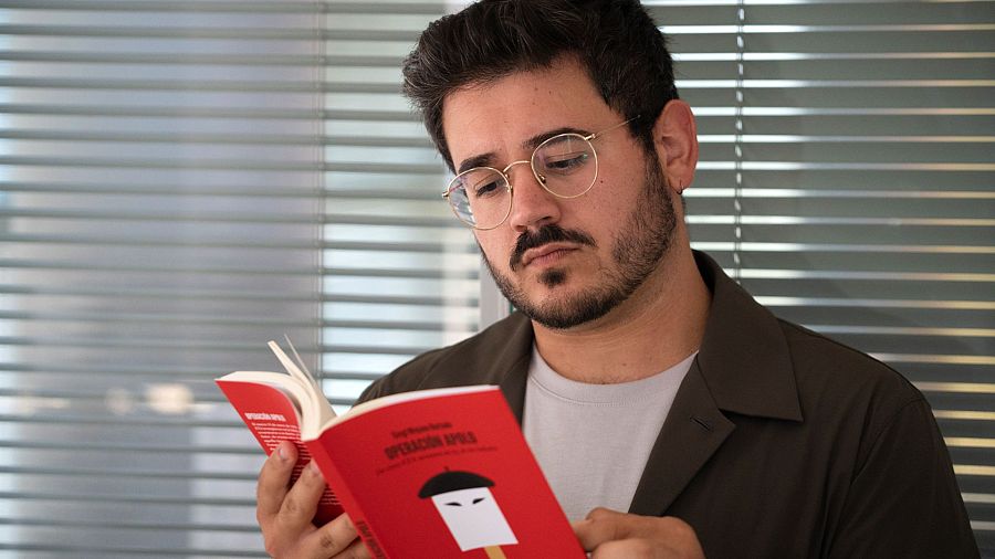 Hombre con gafas leyendo un libro rojo titulado 