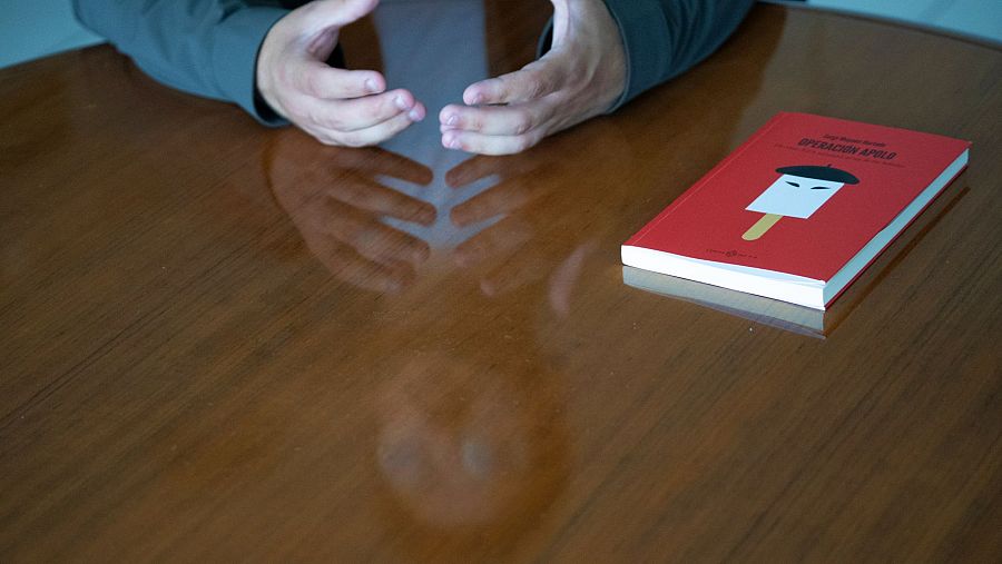 Entrevista a Sergi Moyano en Valencia.  Sus manos descansan sobre una mesa de madera pulida, junto a un libro rojo titulado 