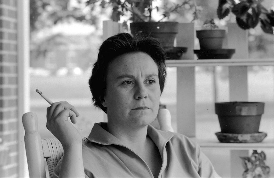 Harper Lee, en foto en blanco y negro, sentada y pensativa, fuma un cigarrillo.  Al fondo, una estantería con macetas.