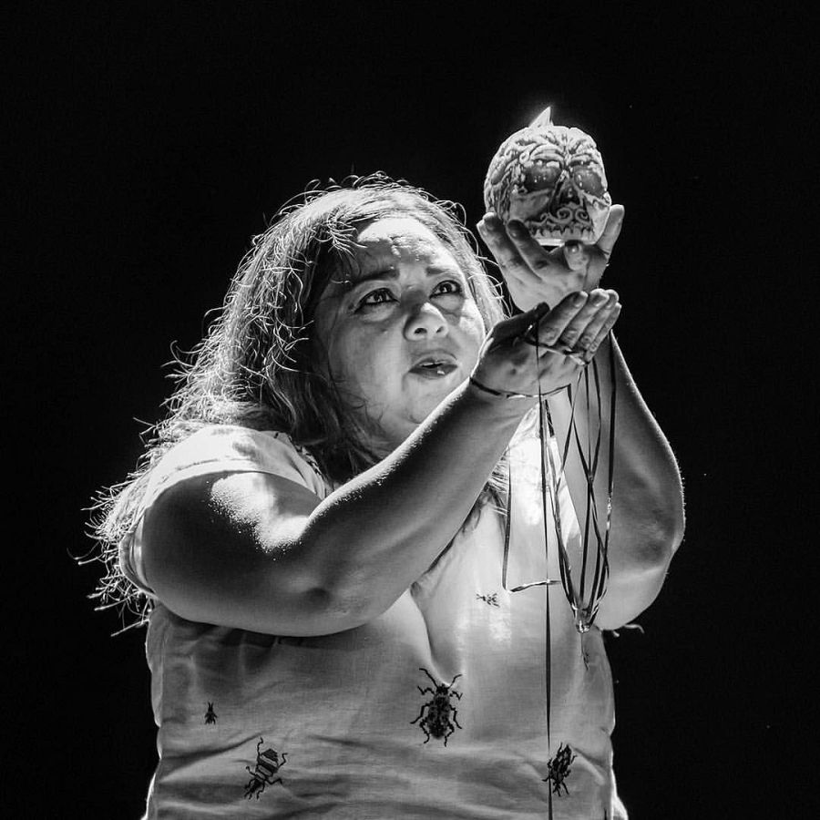 Conchi León, en escena, sostiene una calavera con ambas manos.  Cabello oscuro, camiseta blanca con dibujos. Fondo negro.