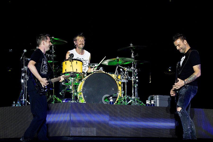 Concierto de Muse en Madrid: Bellamy a la guitarra, Wolstenholme al bajo y Howard en la batería, sobre un escenario con iluminación azul.