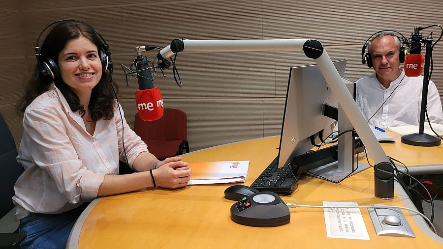 Sesión de grabación en estudio de radio: dos personas con auriculares frente a micrófonos RNE.  En la mesa se observa un ordenador, mesa de mezclas y un documento con el logo RNE.