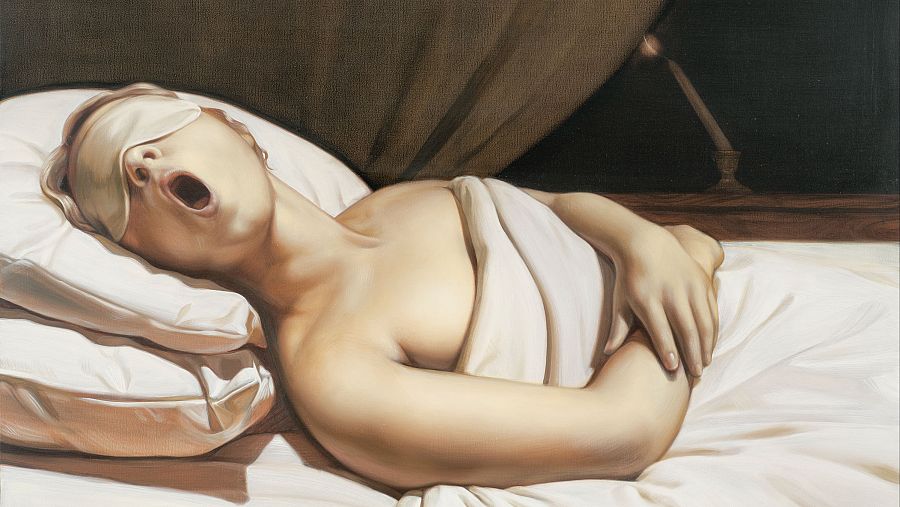 Persona dormida con antifaz en cama con almohadas y sábana blanca; al fondo, cortina oscura y lámpara en mesita de noche.