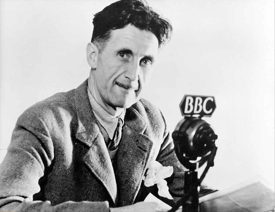 George Orwell, en blanco y negro, sentado ante un micrófono de la BBC;  parece leer de un documento mientras habla o es entrevistado.