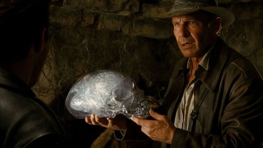 Indiana Jones, interpretado por Harrison Ford, estudia con detalle una calavera de cristal en un entorno oscuro y misterioso.