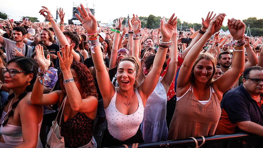 Público eufórico en un concierto, con gente bailando, cantando y grabando; ambiente festivo y mucha energía.