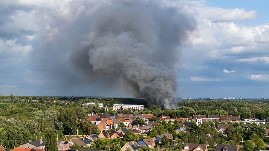 Densa columna de humo gris oscuro sobre zona urbana, vista aérea.  El humo se eleva sobre casas con tejados rojos y marrones, rodeadas de vegetación.