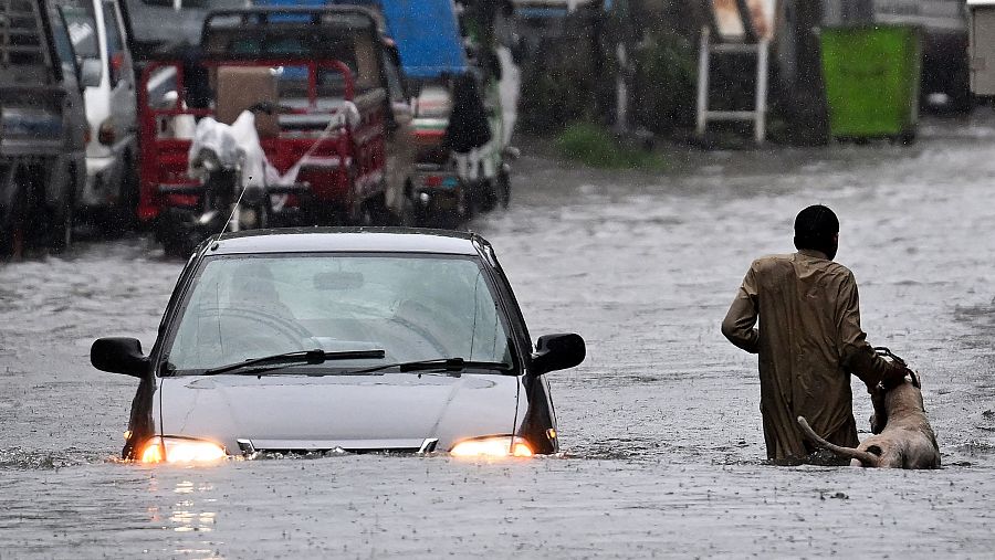 Un hombre junto a su perro mientras un coche vadea una calle inundada durante las fuertes lluvias monzónicas en Rawalpindi, Pakistán