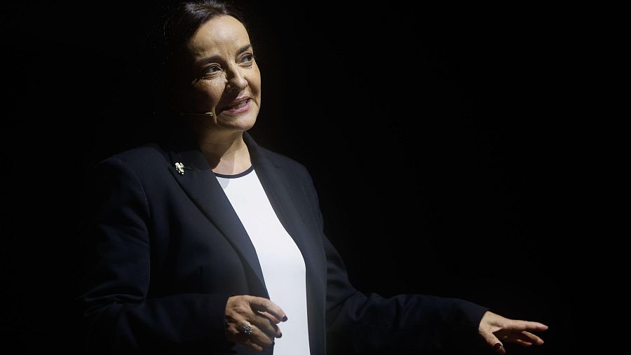 Pepa Bueno, en imagen con fondo oscuro, micrófono y americana, parece presentar o hablar en un programa.