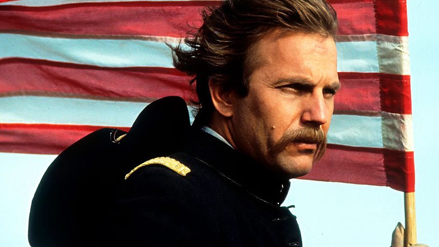 Hombre con uniforme militar y bigote, sujetando una bandera estadounidense, con cita ambiental de proverbio Cree.