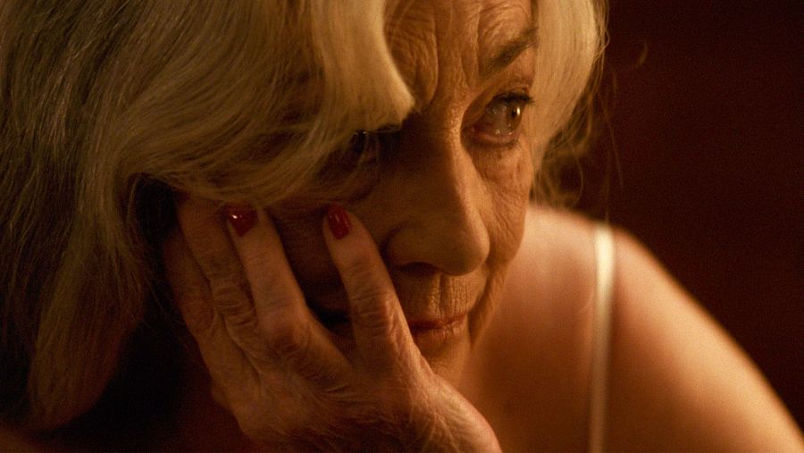 Primer plano de Carmen Maura; expresión seria, mano en mejilla, cabello corto rubio/grisáceo, prenda clara.  Imagen de material de prensa.