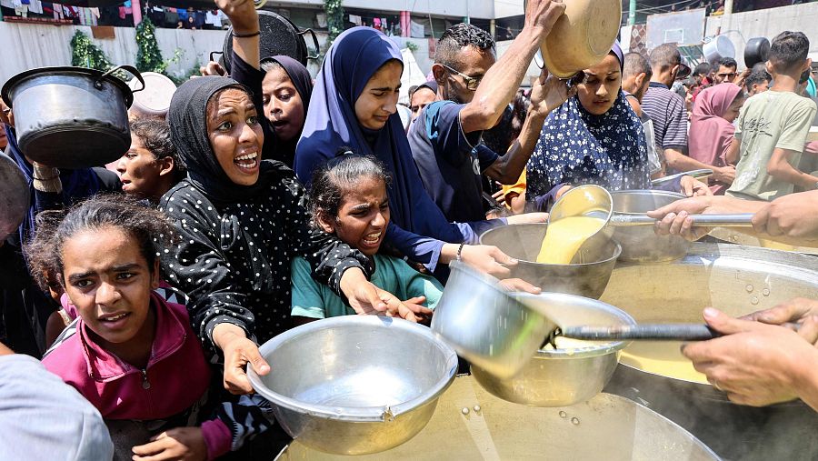 Palestinos desplazados reciben sopa de lentejas en un punto de distribución en Gaza
