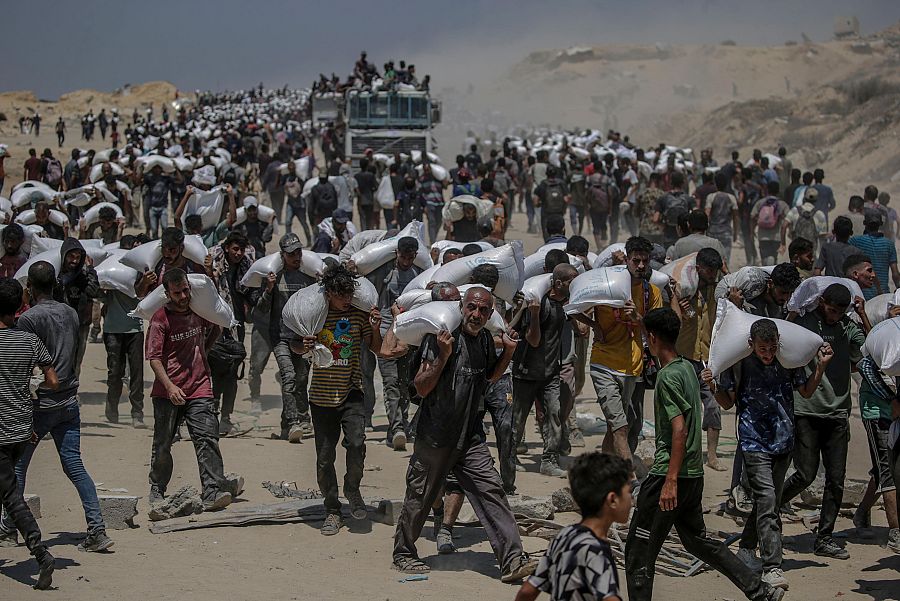 Palestinos portan sacos de harina cerca de un punto de distribución de alimentos en Zikim, al norte de la Franja de Gaza