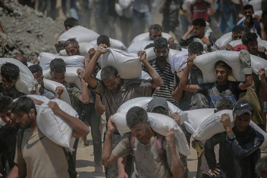 Gazatíes transportan sacos de harina cerca de un punto de distribución de alimentos en Zikim, al norte de la Franja de Gaza