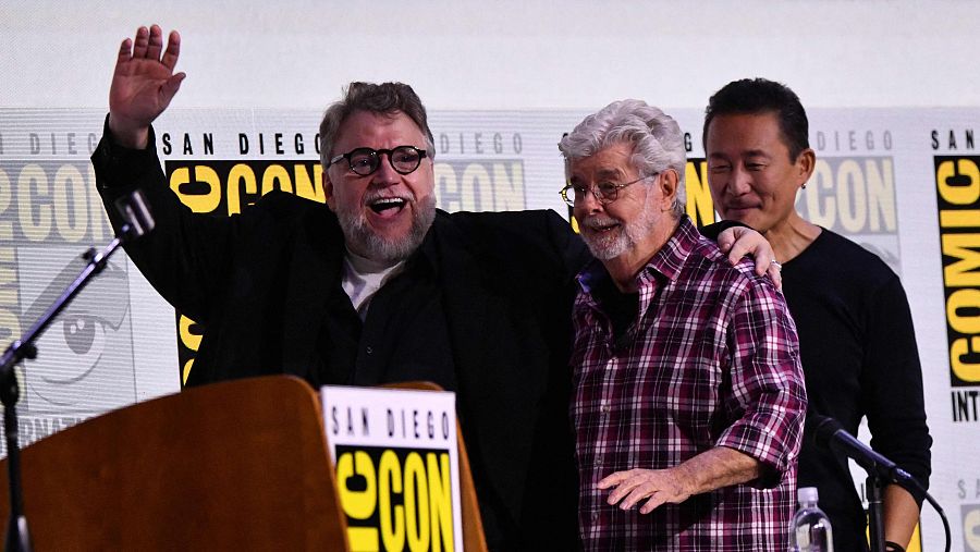 Fotografía de Guillermo del Toro y George Lucas en un escenario, posiblemente durante una presentación en la Comic-Con de San Diego. Del Toro saluda con la mano.