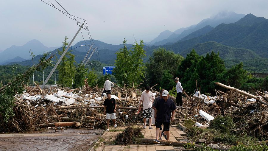 Residentes locales caminan frente a una carretera dañada cubierta de ramas de árboles rotas tras fuertes lluvias en la localidad de Taishitun, distrito de Miyun, en las afueras de Pekín, China.