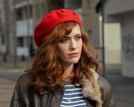 Izaskun Bergara, con boina roja y chaqueta de cuero, mira hacia la derecha.  Cabello rizado rojizo y camiseta a rayas. Fondo desenfocado.