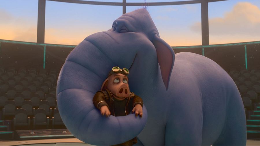 Cerdo con gafas y chaqueta abrazado por un elefante azul en escenario circular con asientos vacíos y ventana mostrando un cielo anaranjado.