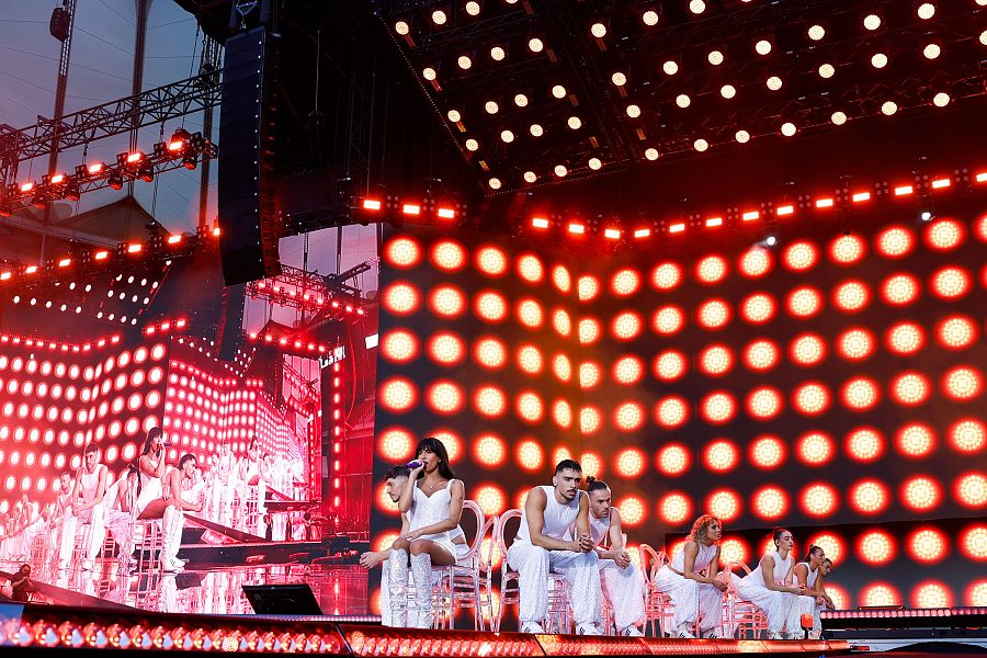 Cantante en escena con bailarines, todos vestidos de blanco, bajo luces rojas.  Ambiente de complicidad durante la actuación.