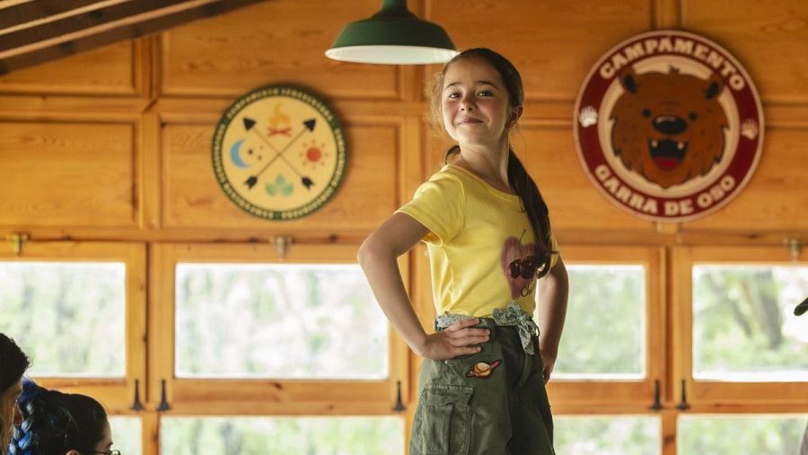 Niña en cabaña de madera con decoración circular de un oso y el texto 