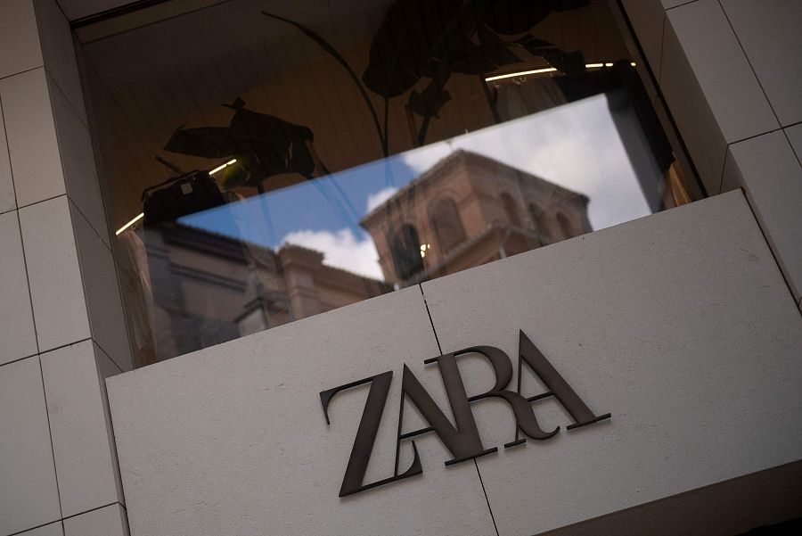 Logo de Zara en fachada de tienda con baldosas claras.  El escaparate refleja un edificio histórico, sugiriendo una ubicación céntrica.